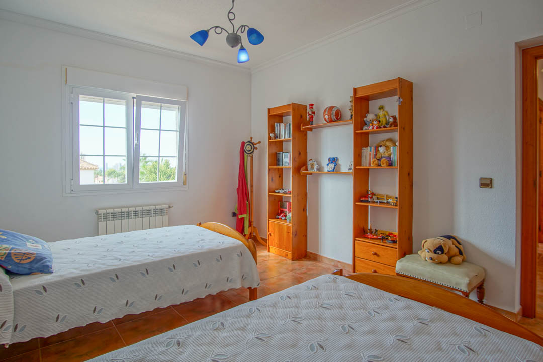 Helles Schlafzimmer mit zwei Einzelbetten, Regalen aus Massivholz und Terrakotta-Fliesenboden. Ein Heizkörper befindet sich unter dem Fenster.