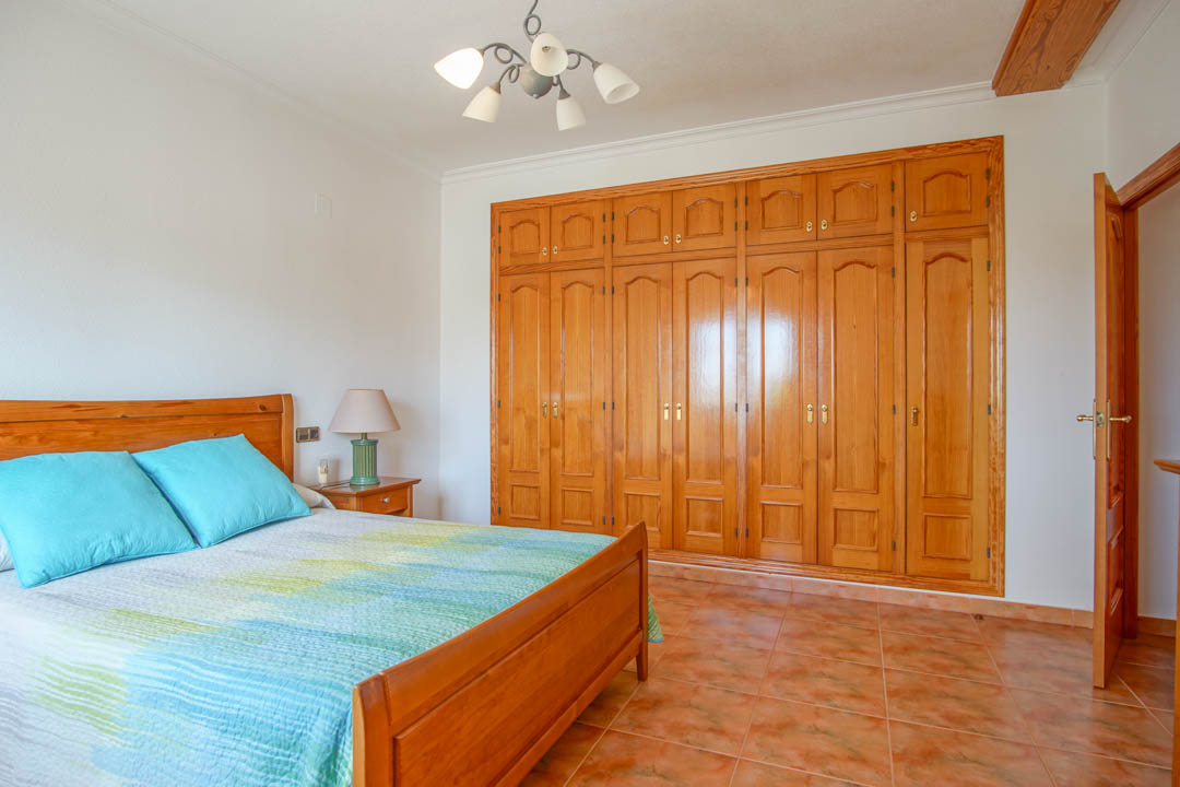Schlafzimmer mit einem großen, maßgefertigten Einbauschrank aus Massivholz, passendem Holzbettrahmen und klassischen Keramikfliesen.