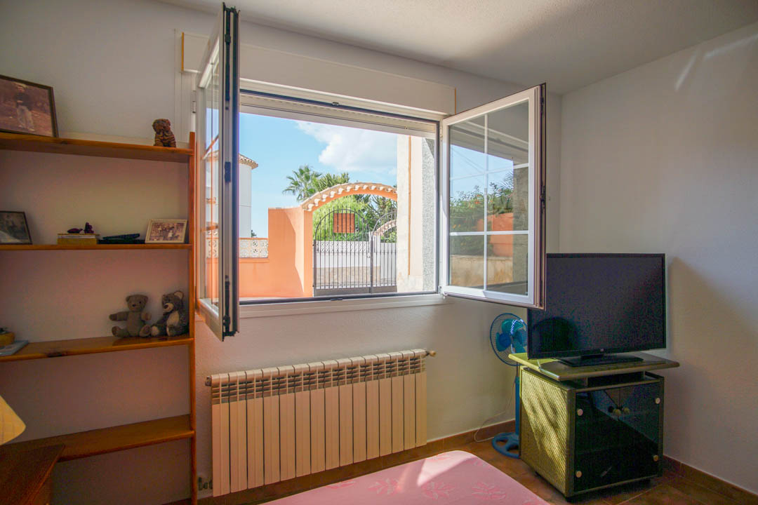 Schlafzimmer mit geöffnetem Sprossenfenster und Blick auf das Eingangstor, ausgestattet mit einem Heizkörper und Regalen aus massivem Echtholz.