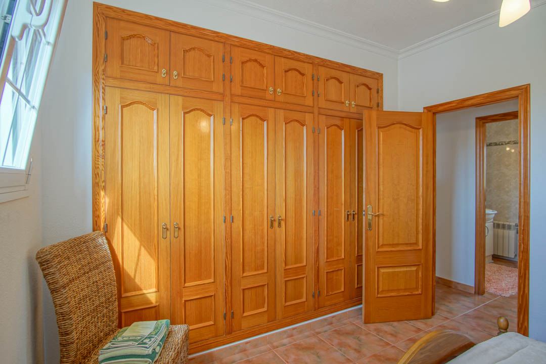 Schlafzimmer mit maßgefertigten Einbauschränken aus Massivholz, Fliesenboden und direktem Zugang zum angrenzenden Badezimmer.