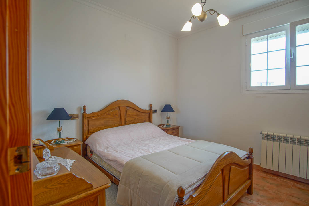 Schlafzimmer mit Massivholzmöbeln, Fliesenboden und weißem PVC-Fenster. Inklusive Heizkörper und klassischen Nachttischlampen auf passenden Holztischen.