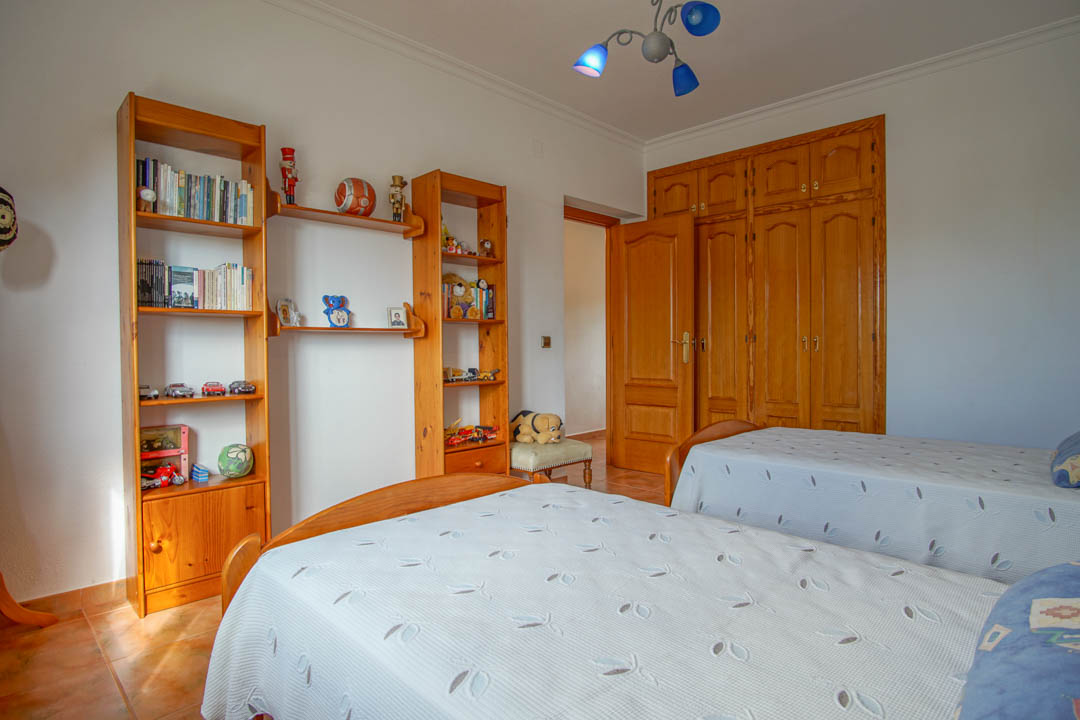 Schlafzimmer mit zwei Einzelbetten, Regalen aus Massivholz und maßgefertigten Einbauschränken mit traditionellen Rundbogen-Fronten.