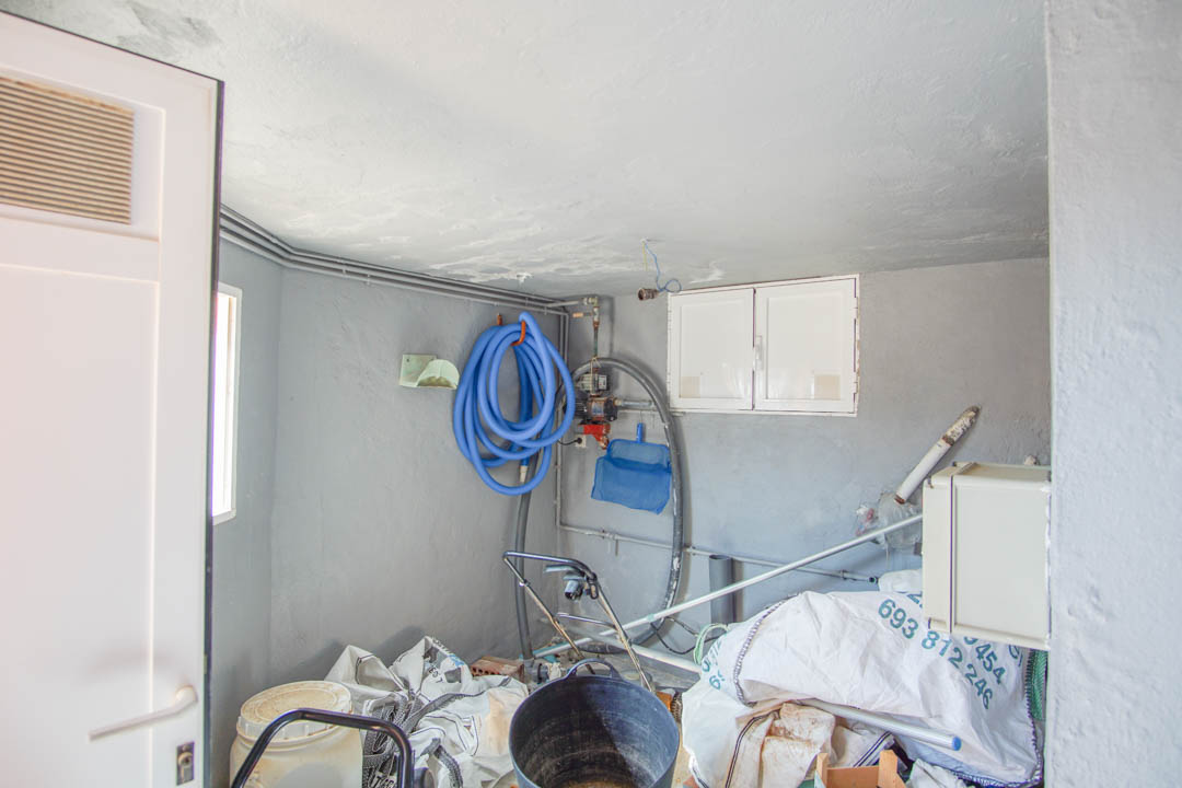 Technik- und Lagerraum mit grauen Wänden, ausgestattet mit blauem Poolschlauch, Reinigungsnetz und integriertem Pumpensystem.