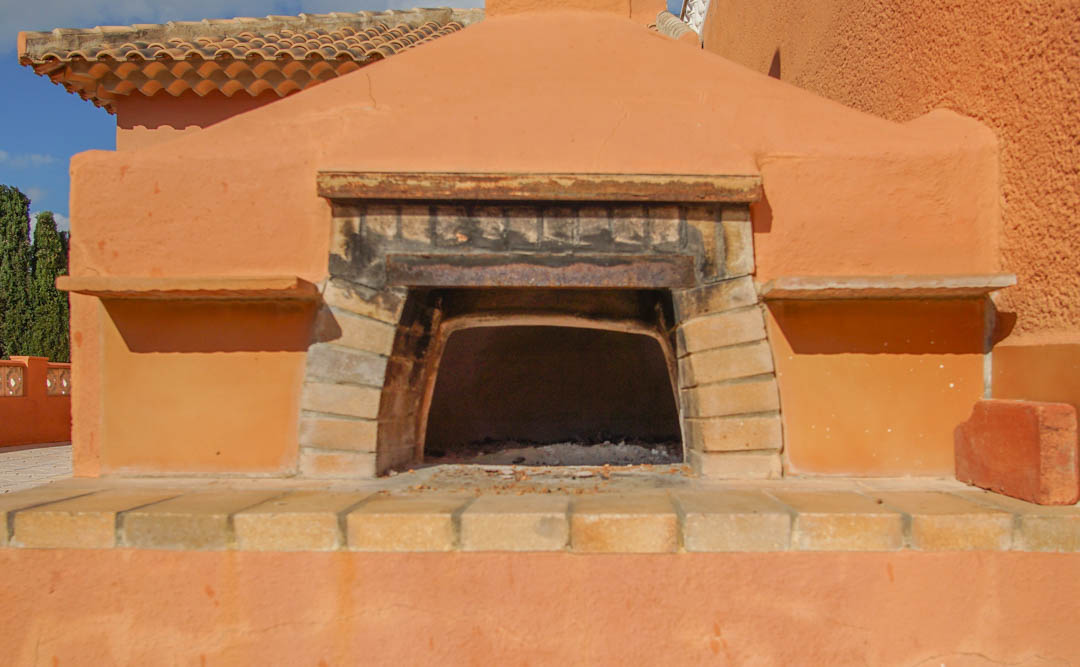Traditioneller Außen-Holzofen, integriert in ein terracottafarbenes Mauerwerk mit Ziegeldetails und einem klassischen Ziegeldach.