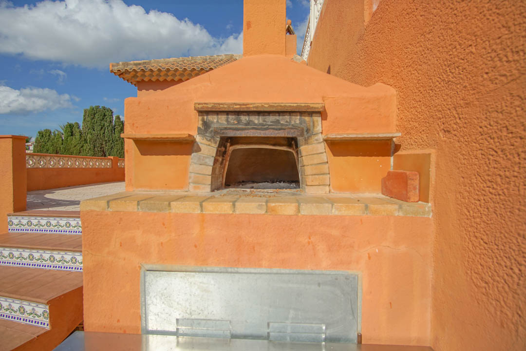 Traditioneller Holzbackofen auf der Außenterrasse mit gemauertem Backsteinbogen und dekorativen mediterranen Fliesen an der angrenzenden Treppe.