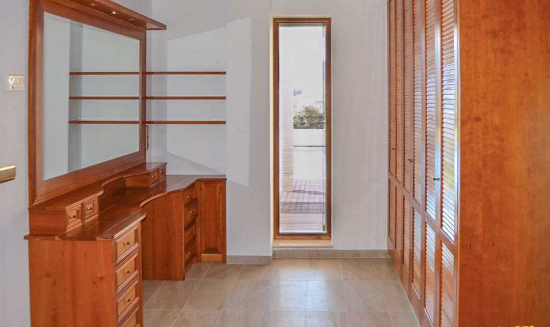 Ankleidezimmer mit hochwertigem Holz-Frisiertisch, Einbauschränken mit Lamellentüren und einem vertikalen Fenster für direktes Tageslicht.
