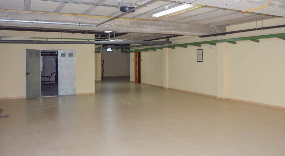 Großzügige Tiefgarage mit Fliesenboden, Sichtbetonbalken an der Decke und integrierten Technikräumen mit industriellen Metalltüren.