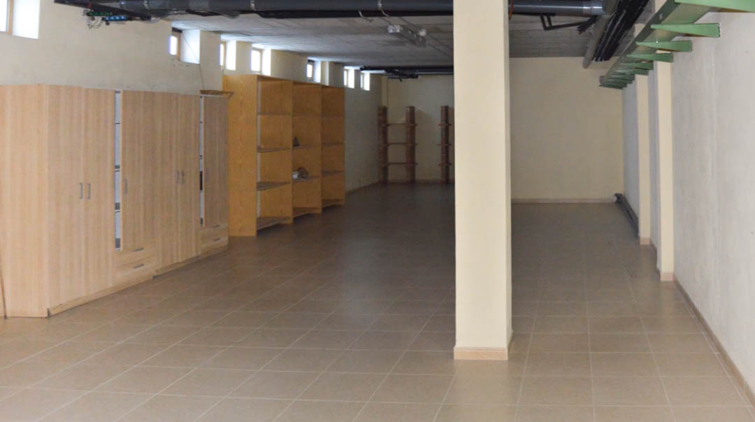 Großzügiger technischer Kellerbereich mit Fliesenboden, Stützsäulen und Holzschränken. Sichtbare Deckeninstallationen und kleine Oberlichter sorgen für Belüftung.