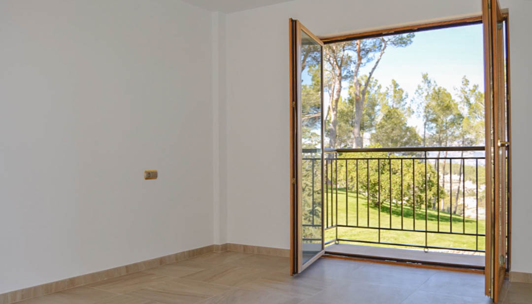 Heller Raum mit Fliesenboden und hochwertigen Holz-Doppeltüren, die auf einen privaten Balkon mit Blick auf den Garten und den umliegenden Pinienwald führen.