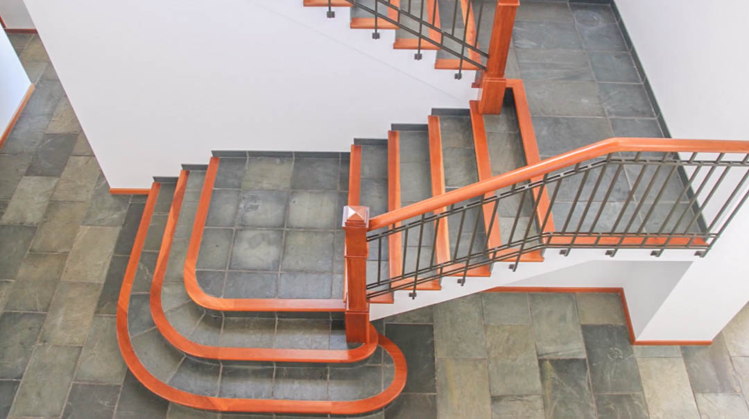 Innentreppe mit Natursteinstufen und edlen Holzkanten. Die Gestaltung umfasst ein dunkles Metallgeländer mit Holzhandlauf auf einem Boden aus Naturschieferplatten.