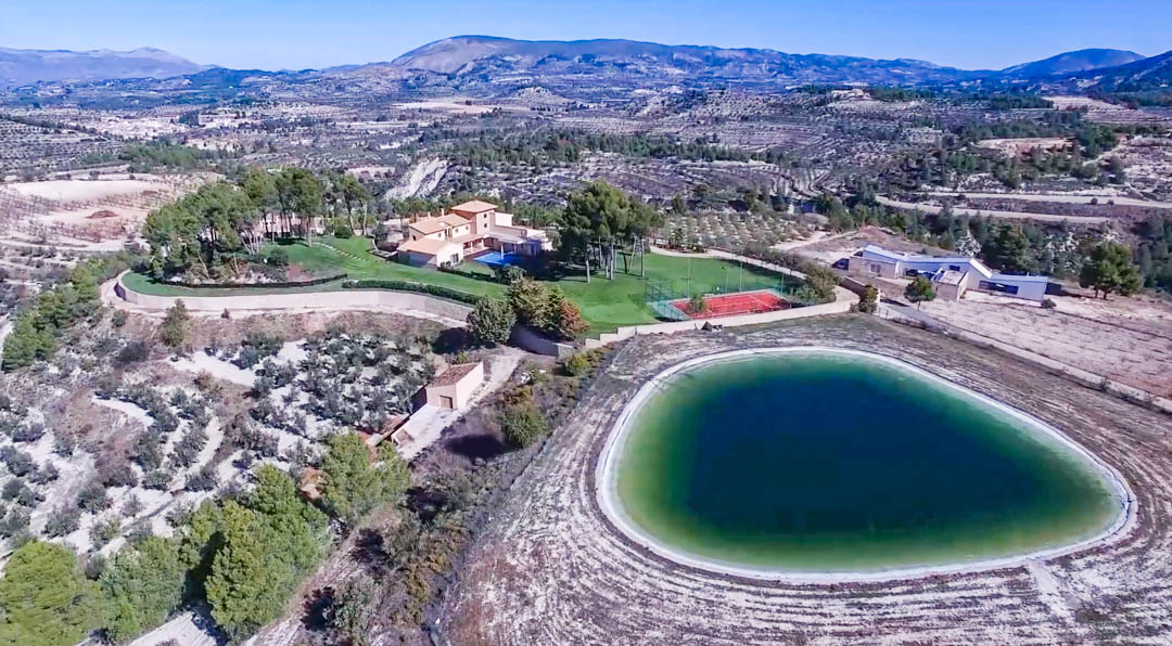 Luftaufnahme des Anwesens mit der Hauptvilla, dem Pool, dem Tennisplatz und einem großen privaten Reservoir inmitten von Olivenhainen und Bergketten.