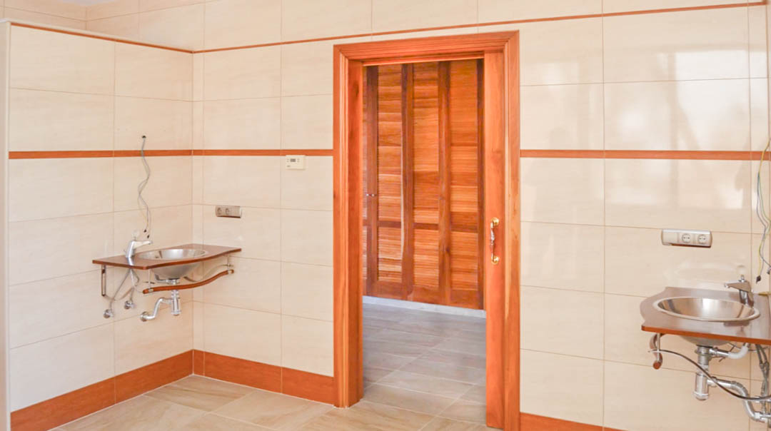 Vorbereitungsraum mit gefliesten Wänden, zwei Edelstahlwaschbecken auf Holzstützen und Durchgang zu einem Raum mit hochwertiger Holzvertäfelung.