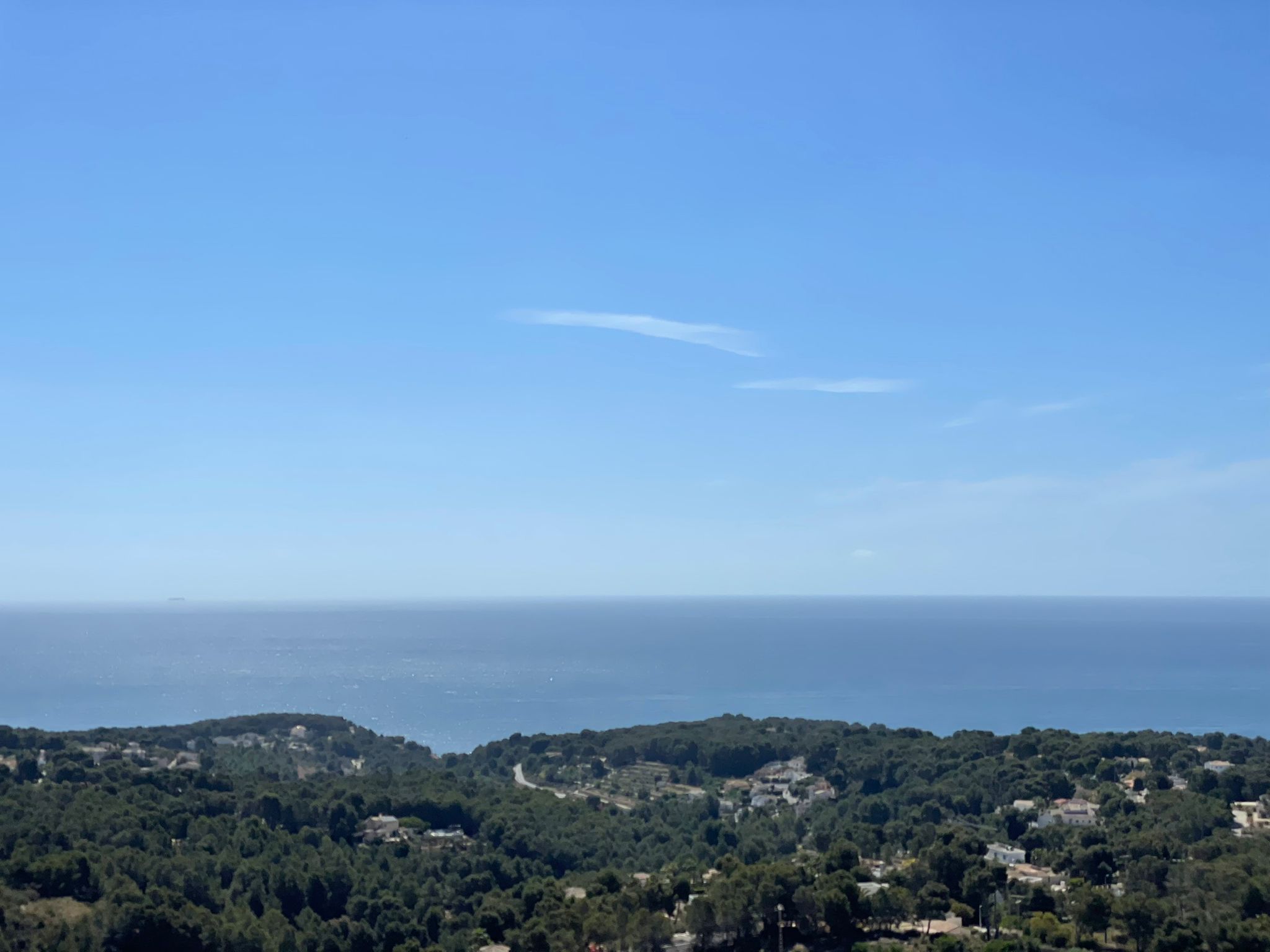 Erhöhter Panoramablick über das Mittelmeer und die bewaldeten Hügel von Benissa mit klarem Horizont und strahlend blauem Himmel.