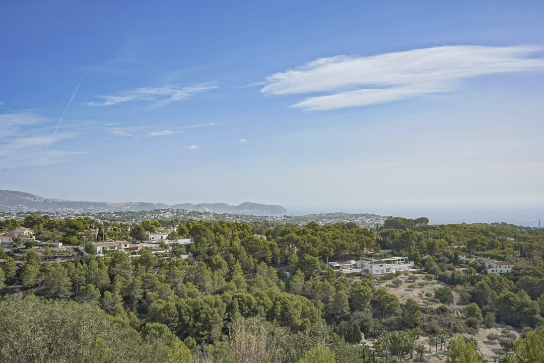 Panoramablick von der Villa auf die Küste von Moraira, mit dem Cap D'or und einer weitläufigen mediterranen Pinienlandschaft unter blauem Himmel.