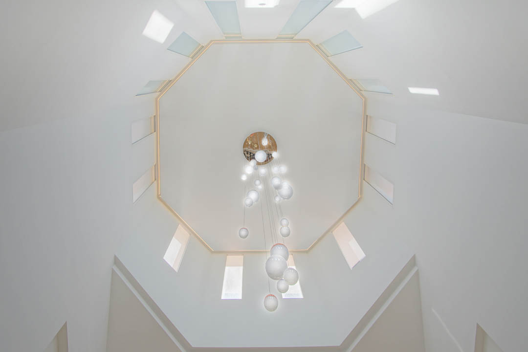 Blick nach oben auf die achteckige Decke mit symmetrischen Oberlichtern und einem modernen Glaskugel-Kronleuchter im doppelstöckigen Treppenhaus.