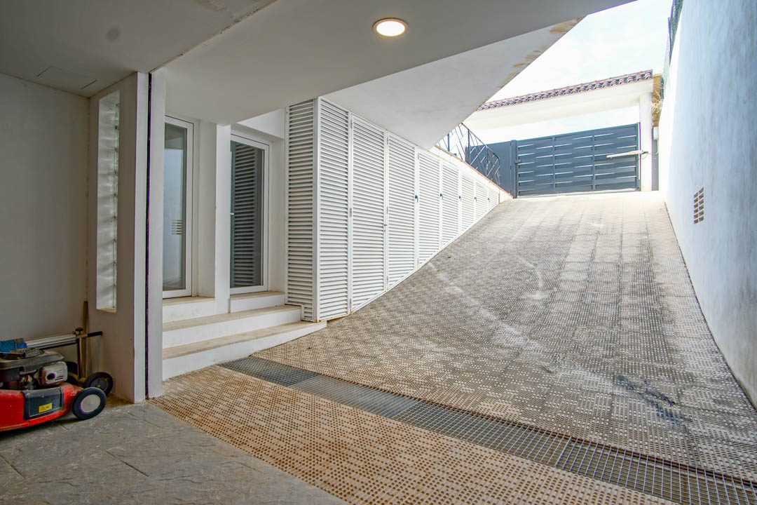 Garagenzufahrt mit rutschfestem Bodenbelag, weißen Lamellentüren für Stauraum und einem Nebeneingang mit Glastüren.