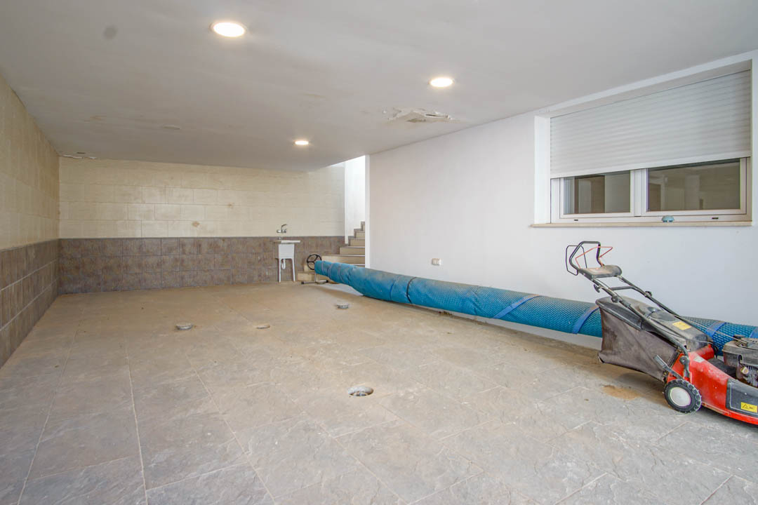 Geräumige Garage mit Keramikfliesen, Einbaustrahlern und einem Waschbecken. Der Bereich bietet direkten Zugang zum Haus und Platz für Gartengeräte.