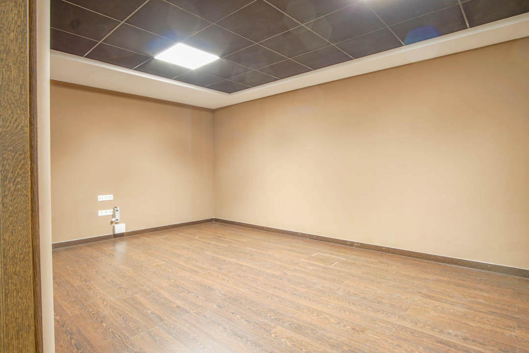 Mehrzweckraum im Untergeschoss mit Boden in Holzoptik, beigen Wänden und einer dunklen Rasterdecke mit integrierter LED-Beleuchtung.
