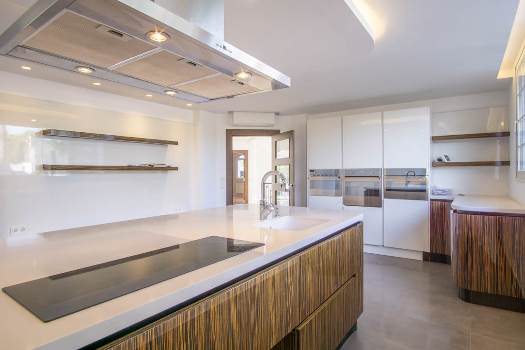 Moderne Küche mit Kochinsel, weißen Arbeitsplatten und Schränken in Holzoptik. Ausgestattet mit integrierten Geräten, Edelstahl-Dunstabzugshaube und schwebenden Regalen.