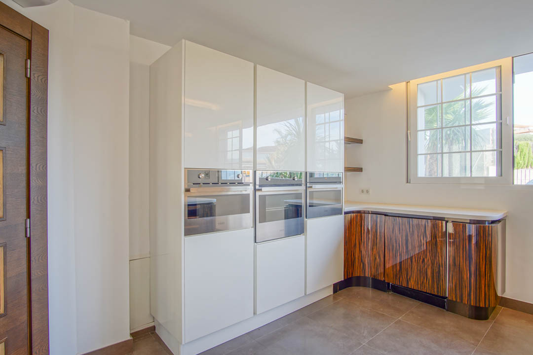Moderne Küche mit weißen Hochglanzschränken, integrierten Edelstahlofen und geschwungenen Unterschränken in markanter dunkler Holzmaserung-Optik.