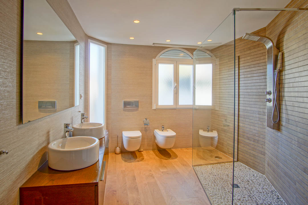 Modernes Badezimmer mit Doppelwaschbecken auf Holzunterschrank, begehbarer Dusche mit Kieselboden und wandhängenden Sanitärobjekten.