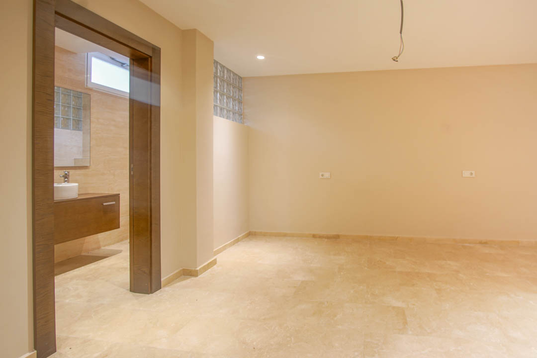 Schlafzimmer mit Natursteinboden und En-Suite-Badezimmer. Ausgestattet mit einem schwebenden Holzwaschtisch, Glasbausteinen und neutralen Wandfarben.
