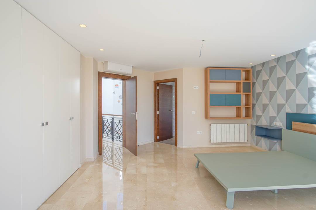 Schlafzimmer mit poliertem Marmorboden, weißen Einbauschränken und einer geometrischen Akzentwand. Ausgestattet mit einem Holzregal und Blick auf den Flurbereich.