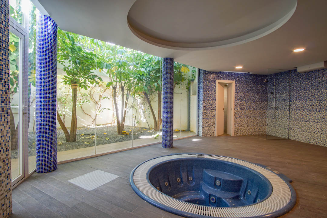 Wellnessbereich mit eingelassenem runden Jacuzzi, blauen Mosaiksäulen und großen Glasfronten mit Blick auf einen begrünten englischen Innenhof.