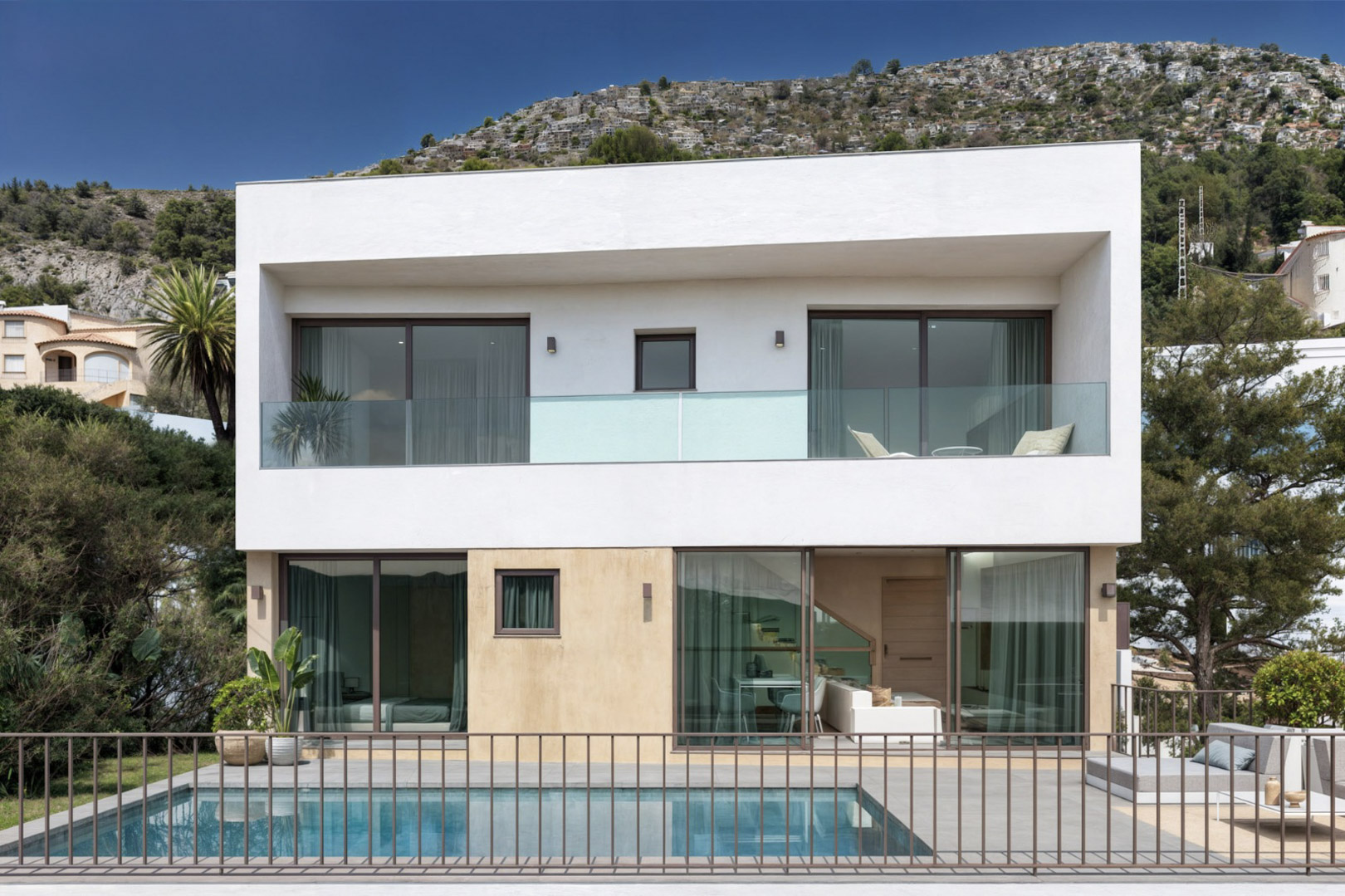 Moderne zweistöckige Fassade mit privatem Pool, bodentiefen Glasfronten und Terrassen mit Glasgeländern, harmonisch in die Hügellandschaft eingebettet.
