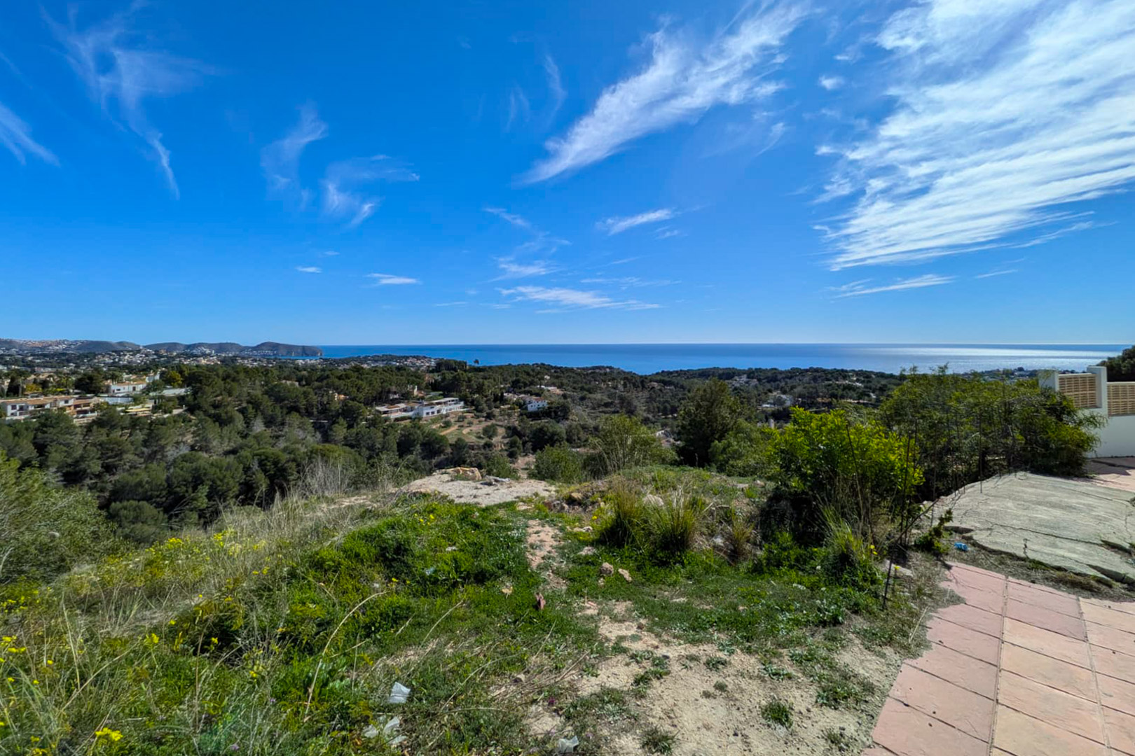 Erhöhter Panoramablick vom Grundstück auf das Mittelmeer, das Cap D'or und die bewaldeten Hügel von Benissa unter blauem Himmel.
