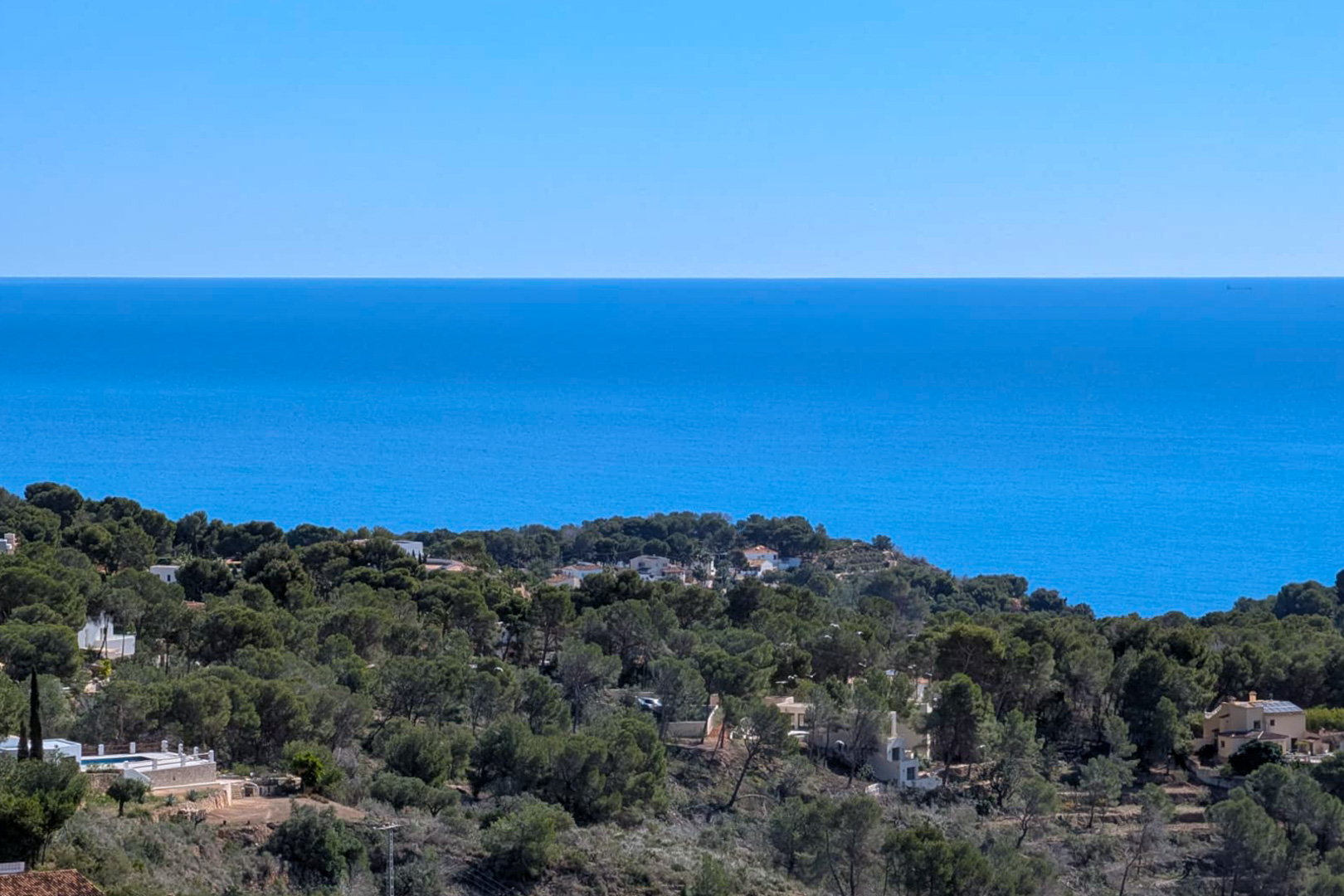 Erhöhter Panoramablick vom Grundstück auf das Mittelmeer und die pinienbewachsenen Hügel von Benissa unter einem klaren blauen Himmel.