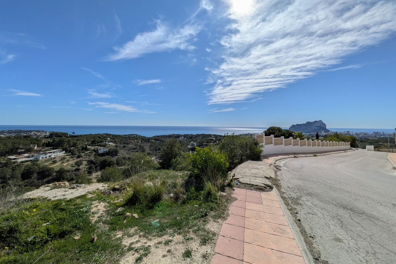 Panoramablick von der Zufahrtsstraße auf die Küste von Benissa, das Mittelmeer und die Silhouette des Peñón de Ifach am Horizont.