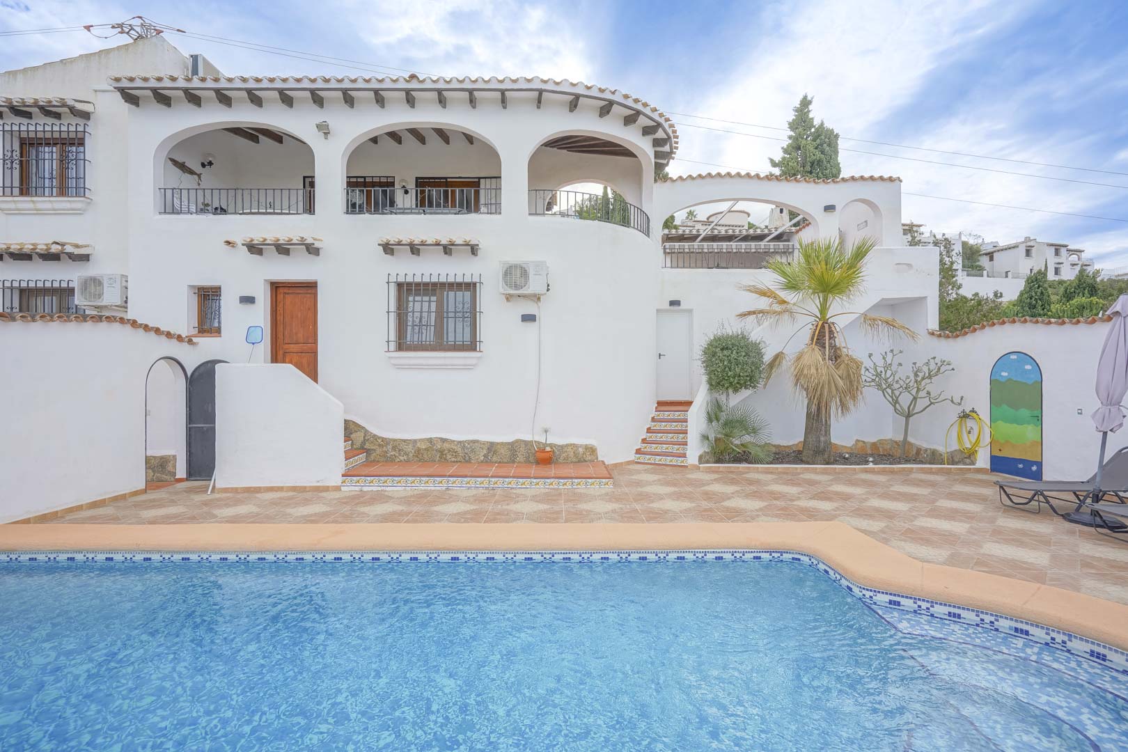 Ansicht der Hauptfassade der Villa mit Pool, gefliester Terrasse und Landschaftsgestaltung.
