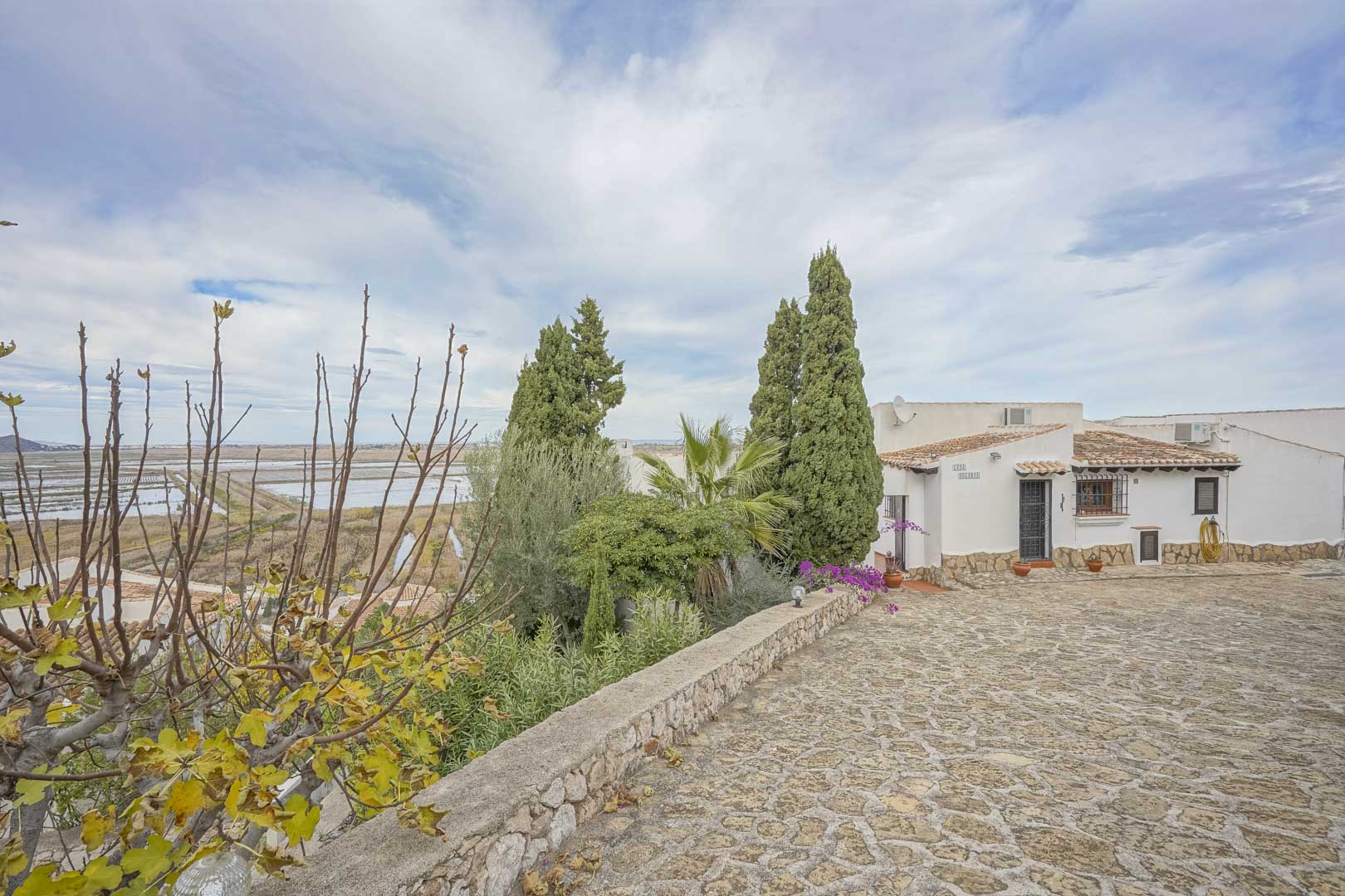Außenansicht der Villa mit gepflasterter Auffahrt, Garten und Panoramablick auf das Naturschutzgebiet.