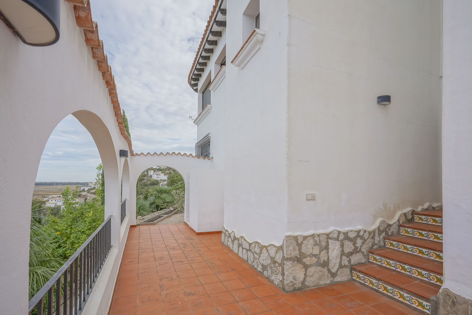 Außenansicht der Villa mit spanischen Bögen, Terrakotta-Terrasse und dekorativer Treppe.
