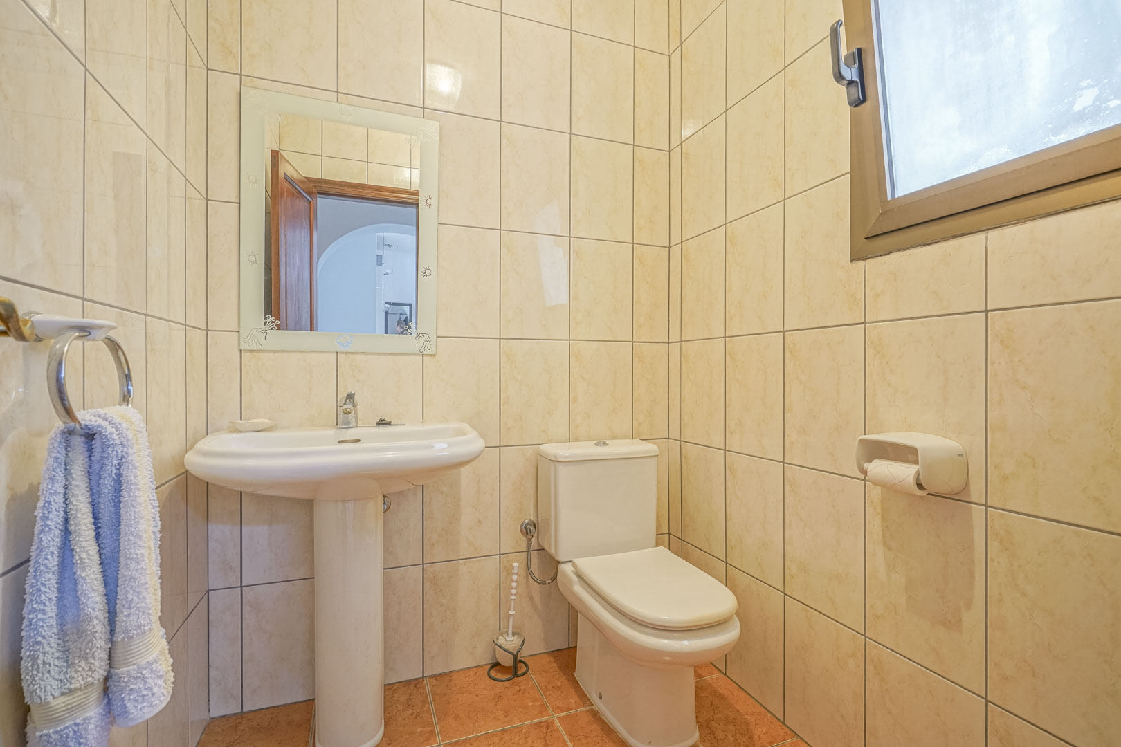 Badezimmer mit cremefarbenen Fliesen, weißem Waschtisch und verziertem Spiegel.