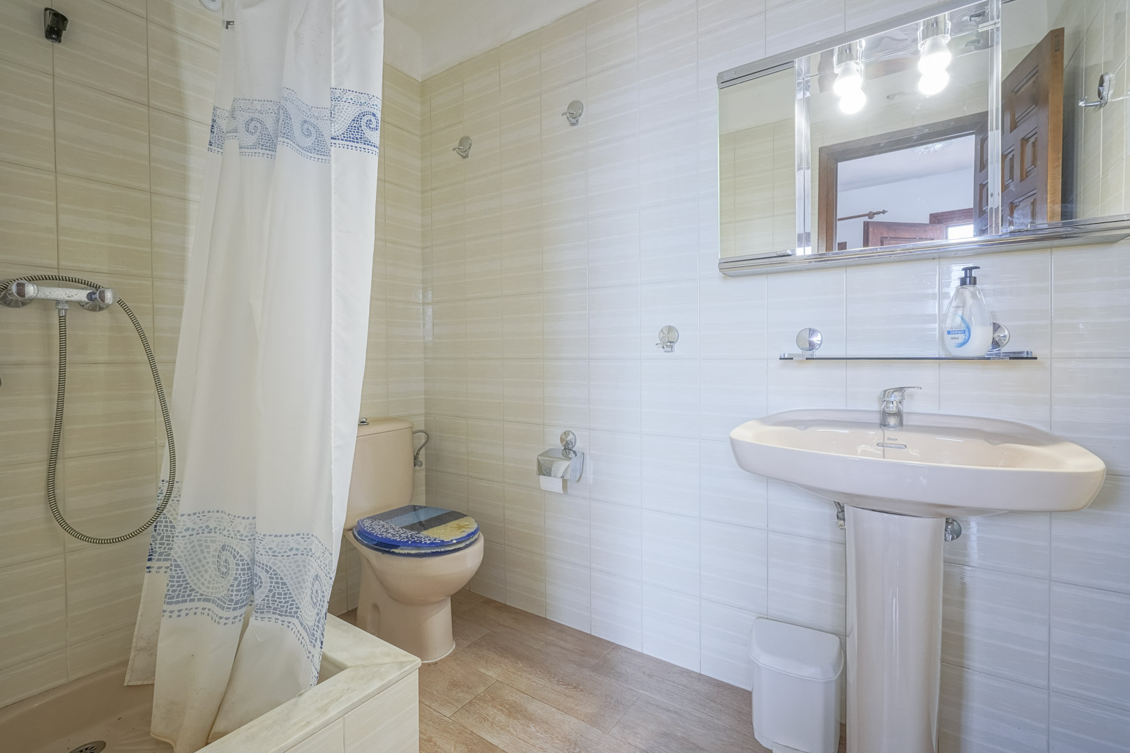 Badezimmer mit hellen Fliesen, einem rosa Waschtisch und einem Duschvorhang mit blauen Mustern.