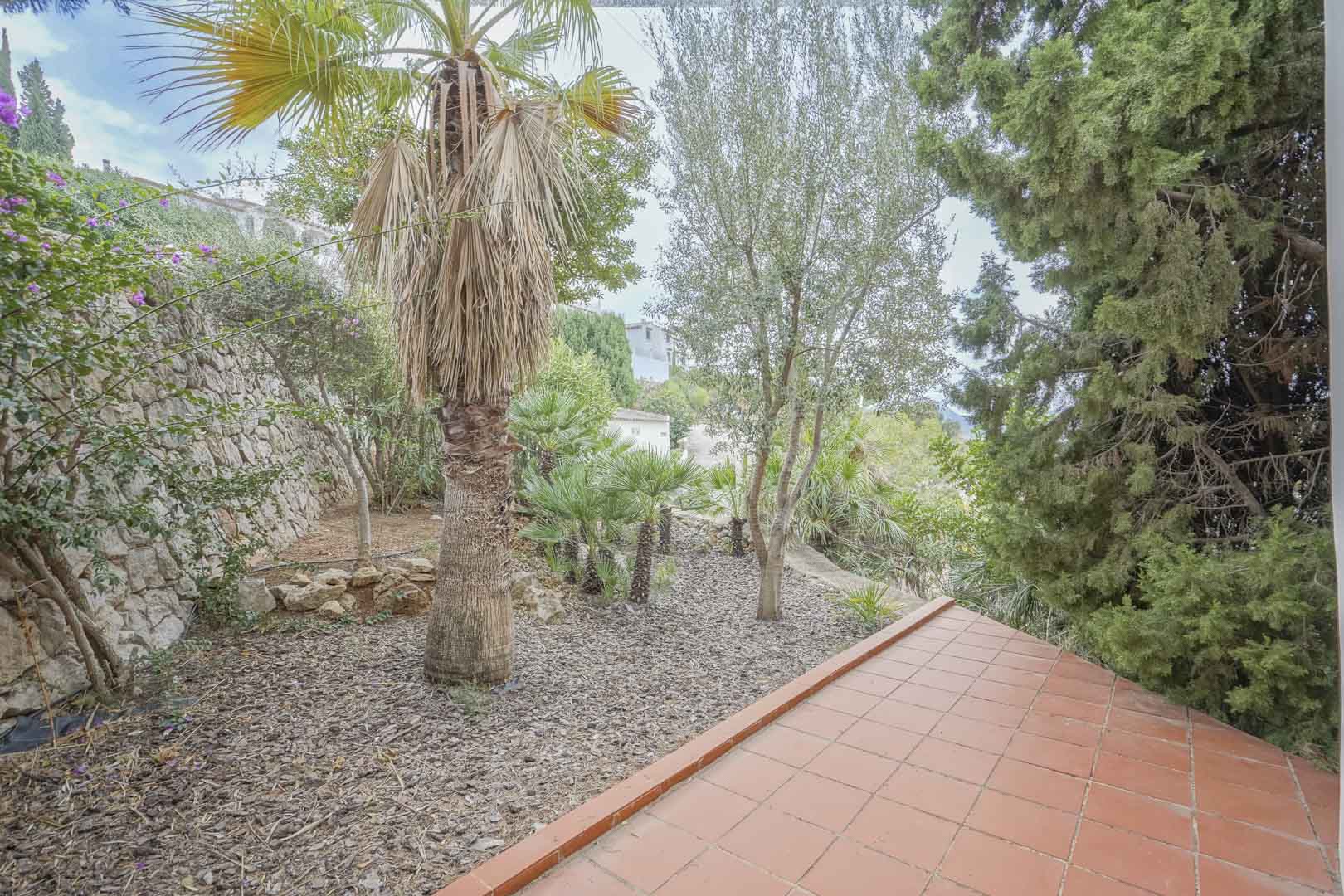 Blick vom der überdachten Terrasse mit Terrakottafliesen auf den pflegeleichten Garten mit automatischer Bewässerung.