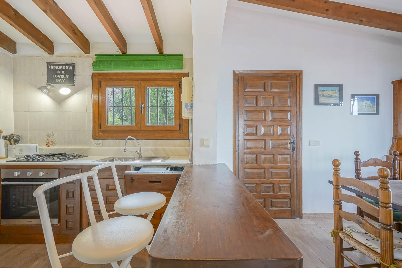 Detailaufnahme der offenen Küche mit Holzbar, weißen Hockern und freiliegenden Deckenbalken.