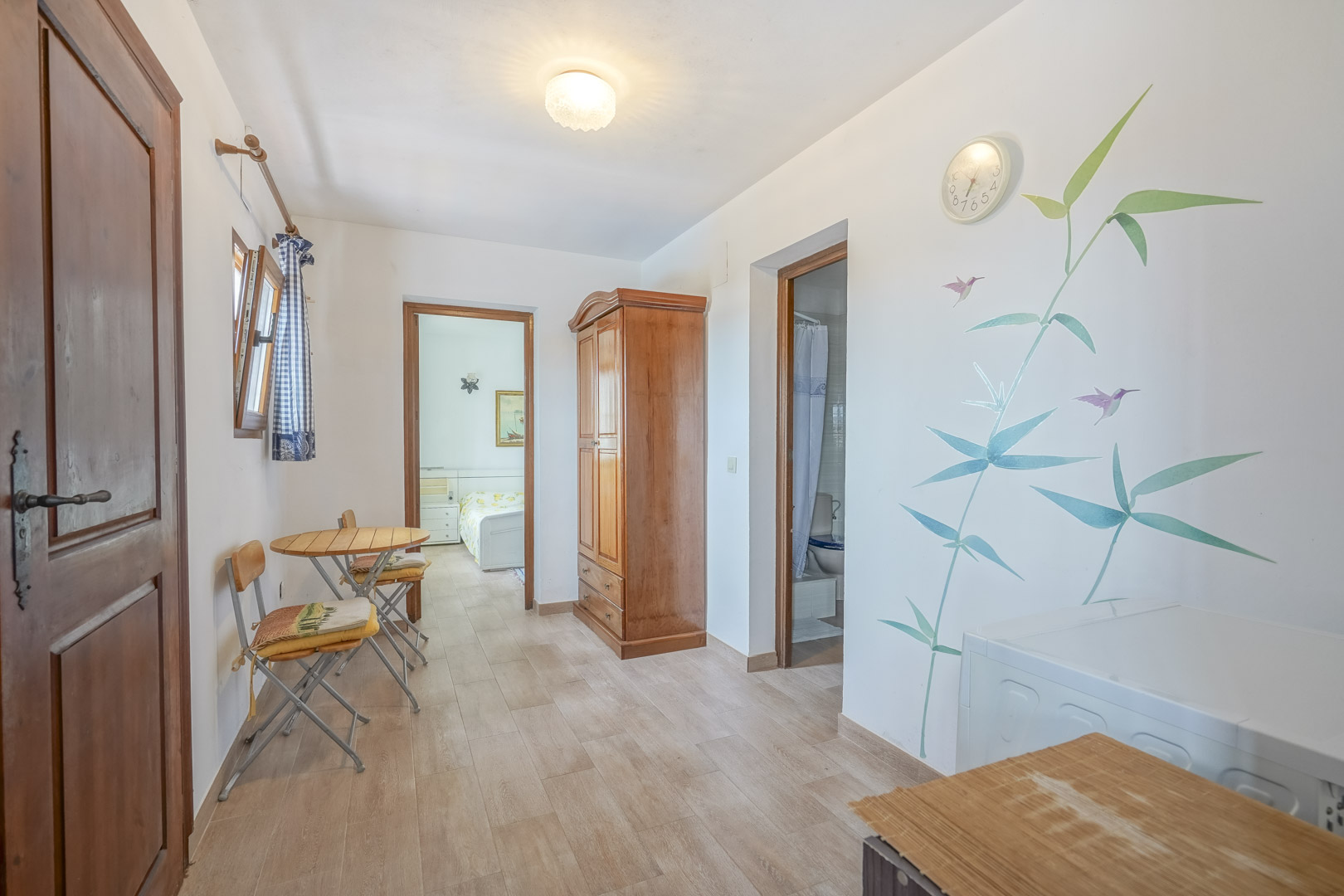 Helles Interieur mit Fliesenboden, Holzschrank und botanischem Wanddekor.