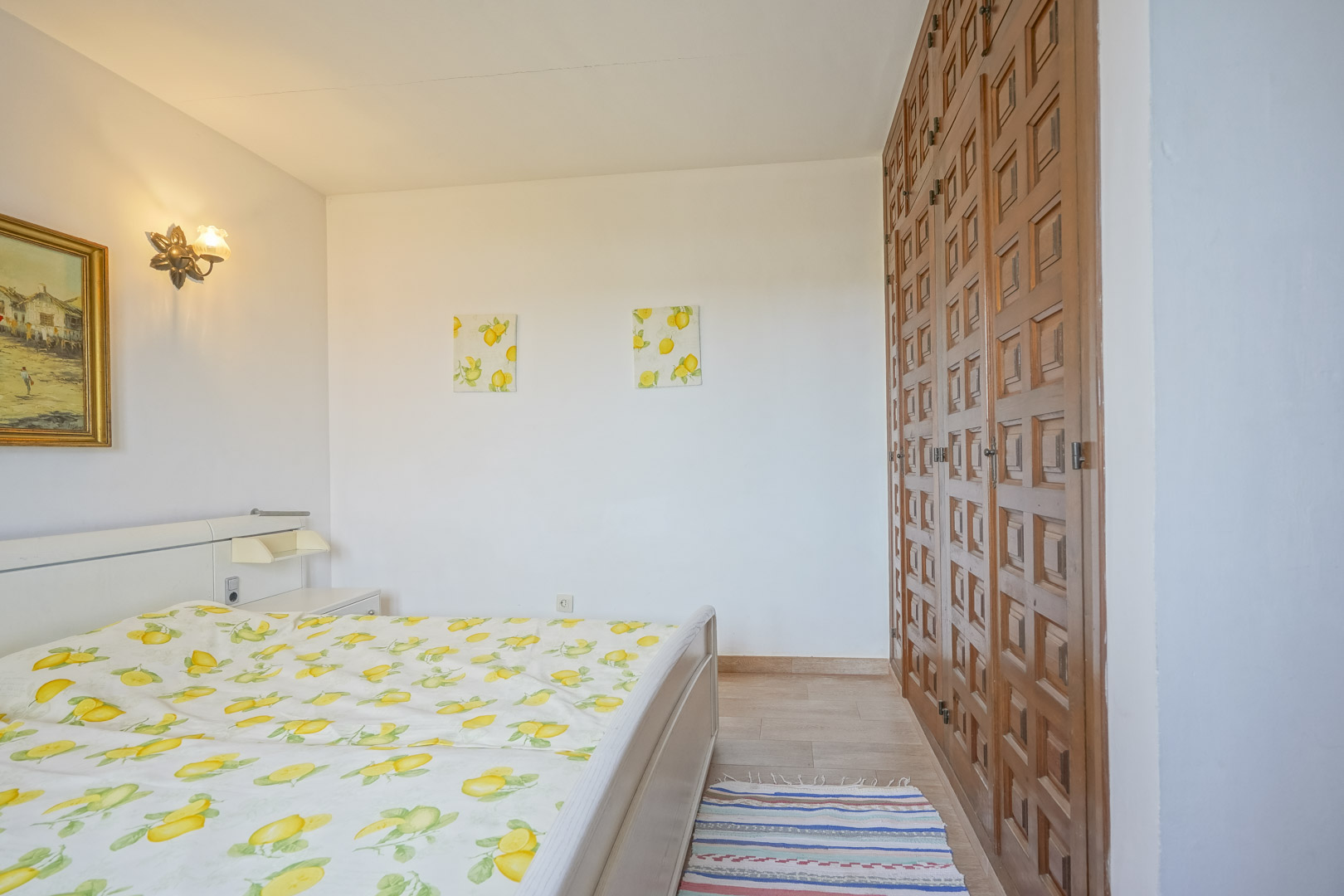 Helles Schlafzimmer mit Bett, Holzschrank und Dekoration mit Zitronenmotiven.