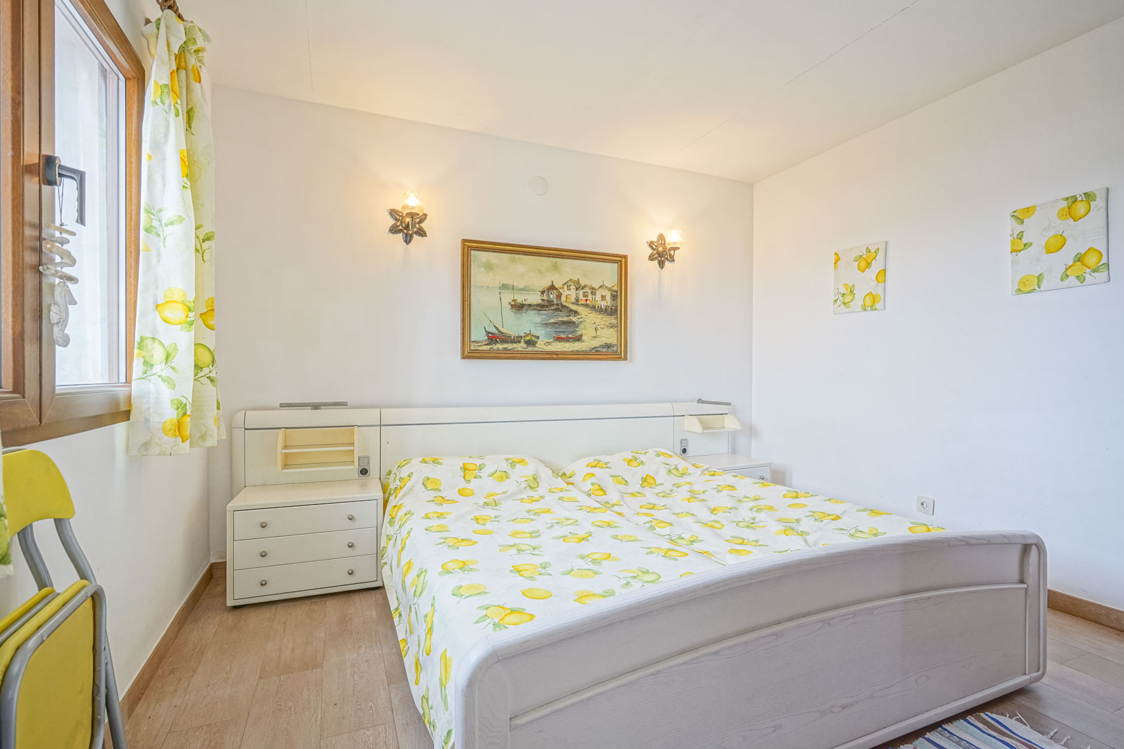 Helles Schlafzimmer mit Doppelbett, weißem Kopfteil mit integrierten Nachttischen und Dekoration mit Zitronenmotiven.