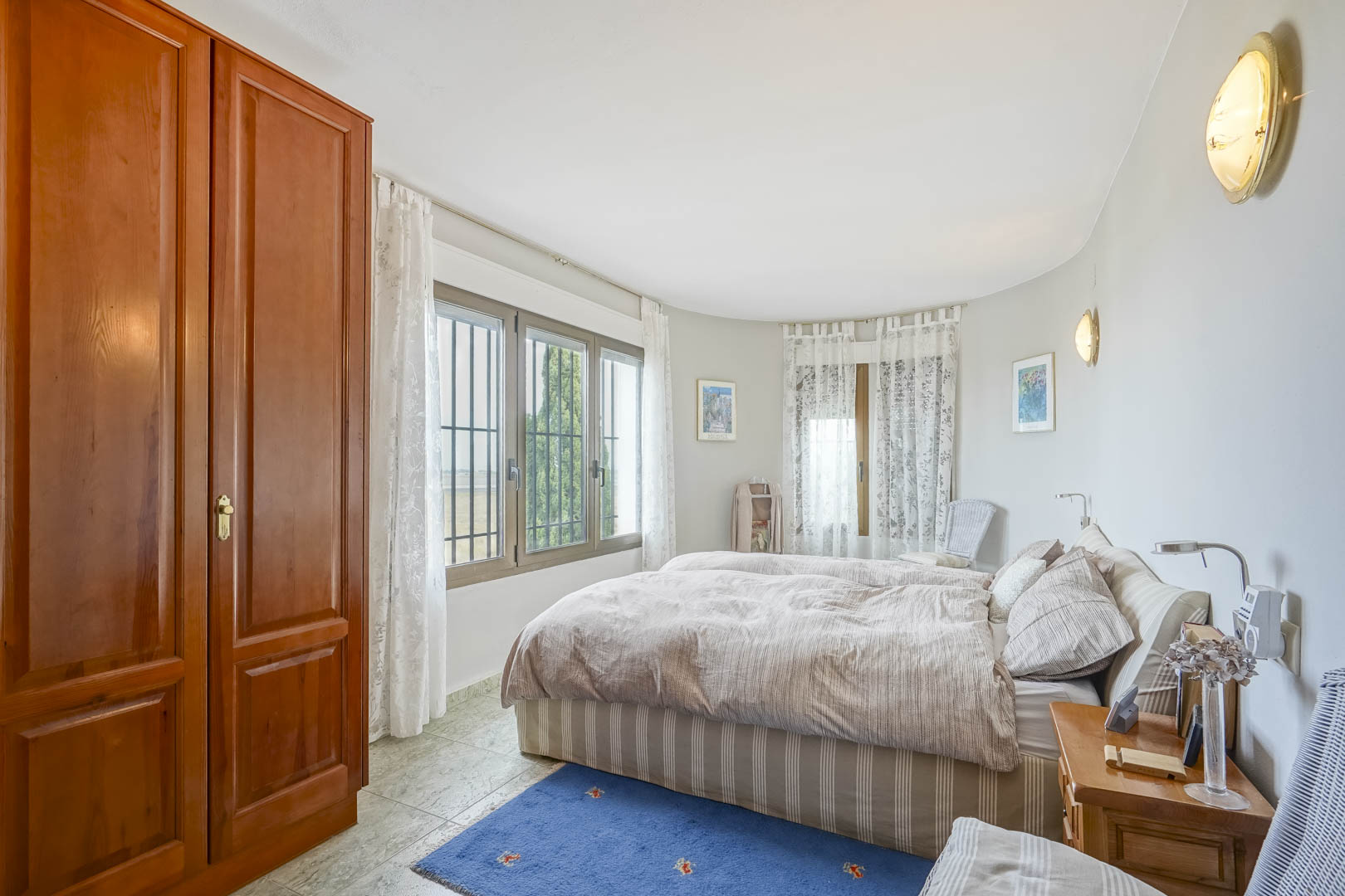 Helles Schlafzimmer mit Holzschrank, Fenstern mit Aussicht und gestreifter Bettwäsche.