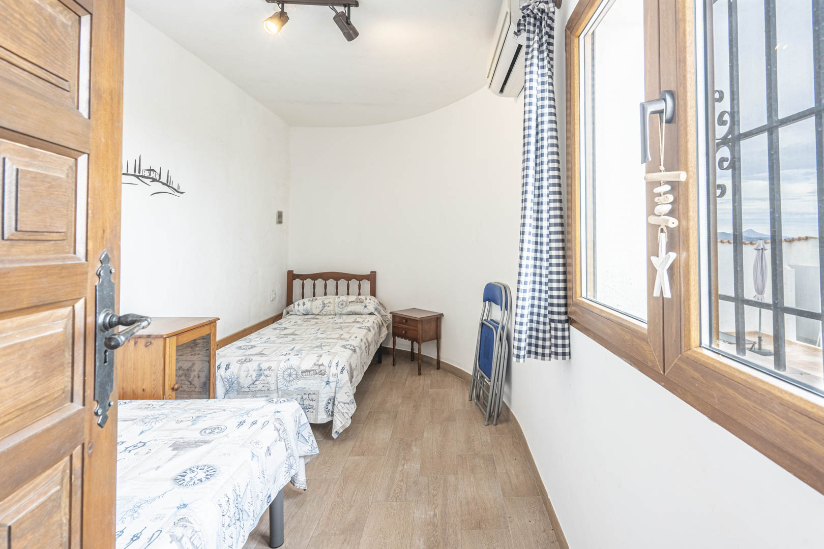 Helles Schlafzimmer mit zwei Einzelbetten, nautischem Dekor und Außenansicht aus dem Holzfenster.