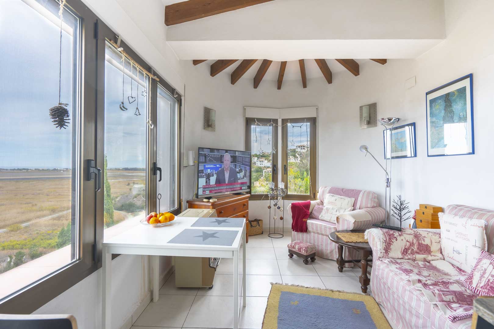 Helles Wohnzimmer mit Holzbalken, gestreiften Sofas und Panoramablick auf die Landschaft.