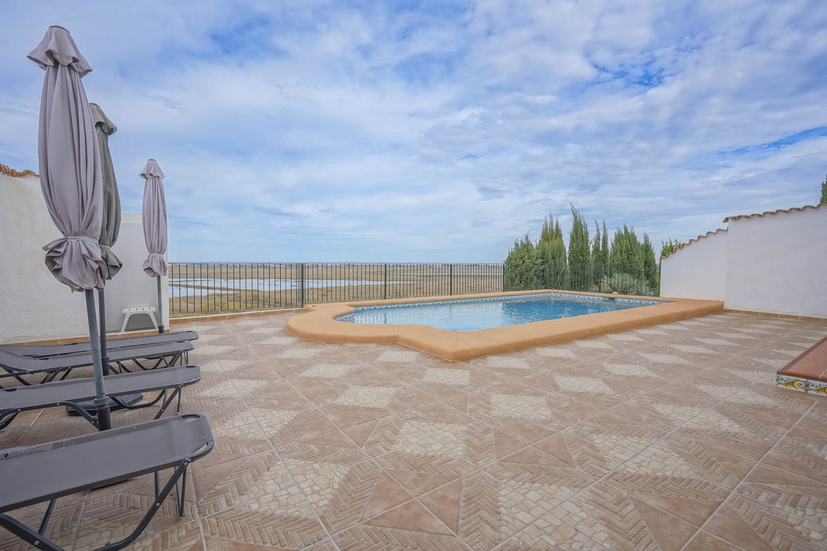 Poolblick mit Liegestühlen und geschlossenen Sonnenschirmen mit Blick auf das Naturschutzgebiet.