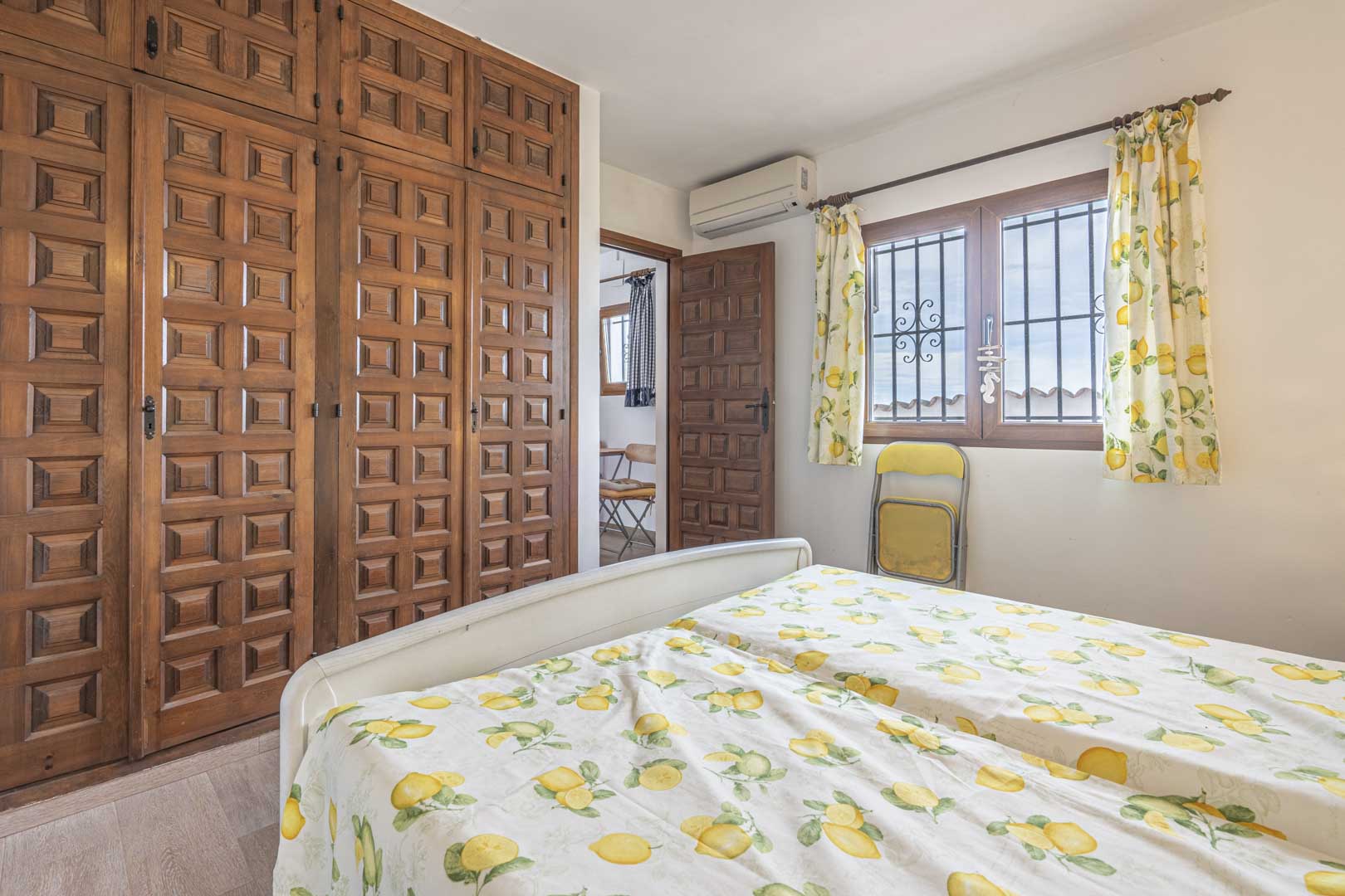 Schlafzimmer mit geschnitztem Holzschrank und Bettwäsche mit Zitronenmuster.