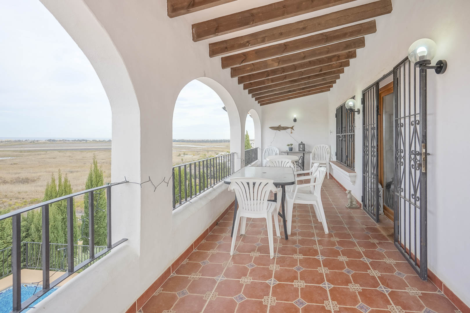 Überdachte Terrasse mit Panoramablick, weißen Bögen und rustikalem Fliesenboden. Gartenmöbel.