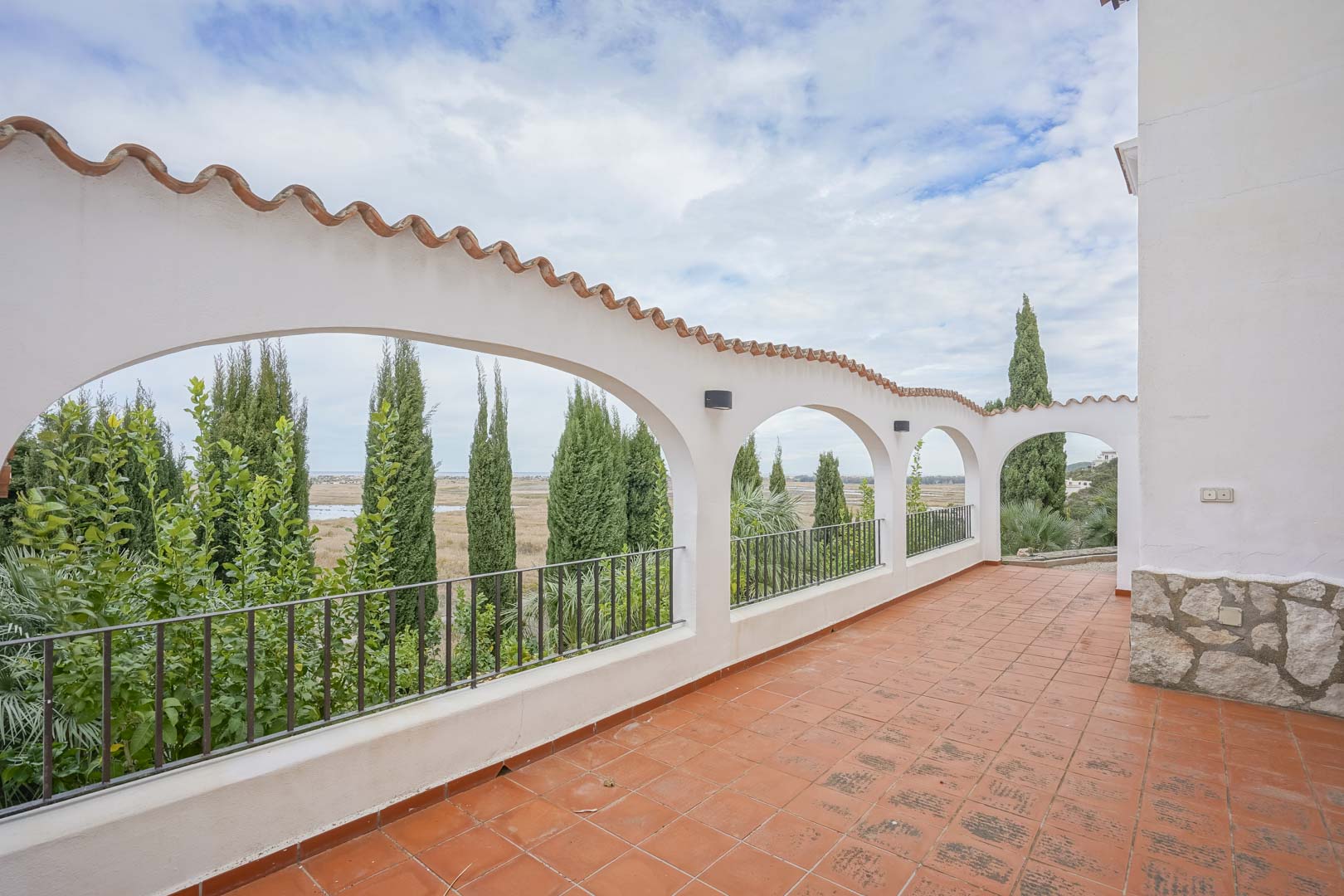 Überdachte Terrasse mit Ziegelbögen und rustikalem Fliesenboden, mit Blick auf Grün und Landschaft.