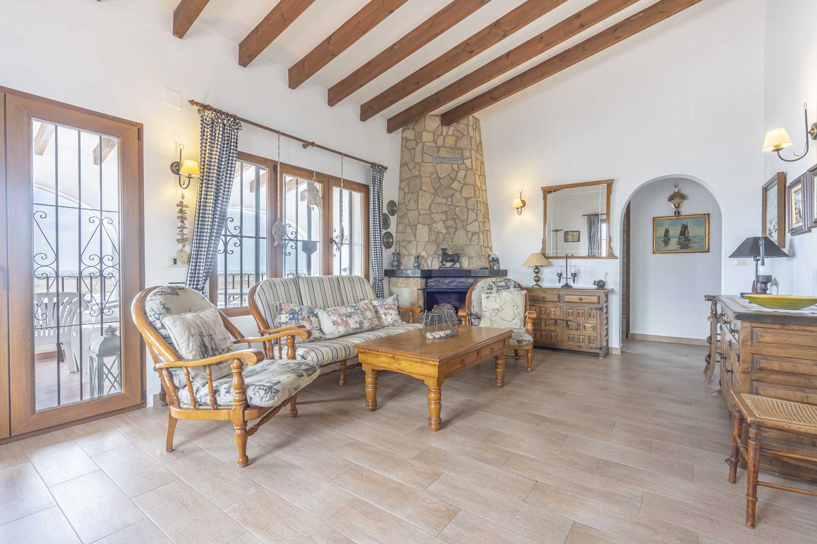 Wohnzimmer mit Steinkamin, Holzbalkendecke und Möbeln im Landhausstil.